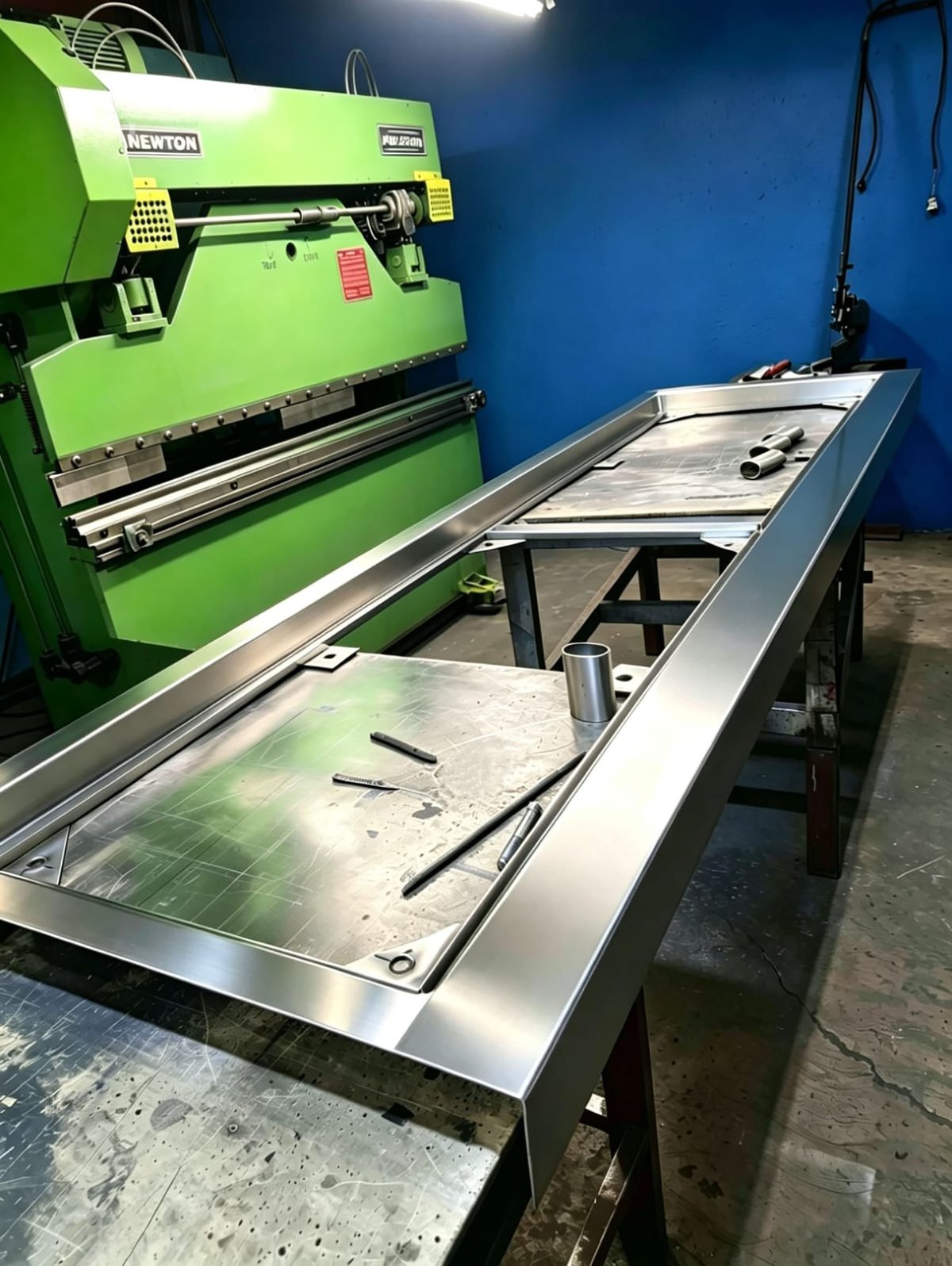 Bright green industrial press brake machine with metal work table in workshop against blue wall
