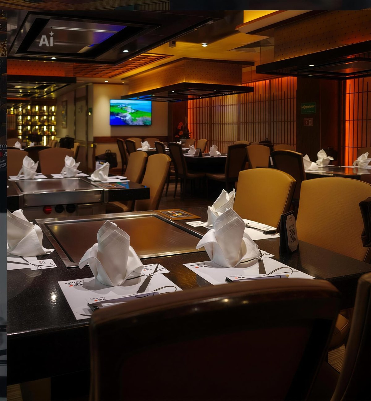 Upscale restaurant dining room with brown tables, gold chairs, white napkins, and warm ambient lighting from ceiling fixtures