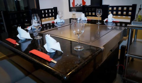 Formal dining table set with wine glasses, napkins, and place settings on dark surface with black chairs