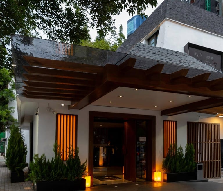 Modern residential entrance with wooden pergola, white walls, warm lighting, and manicured plants at dusk